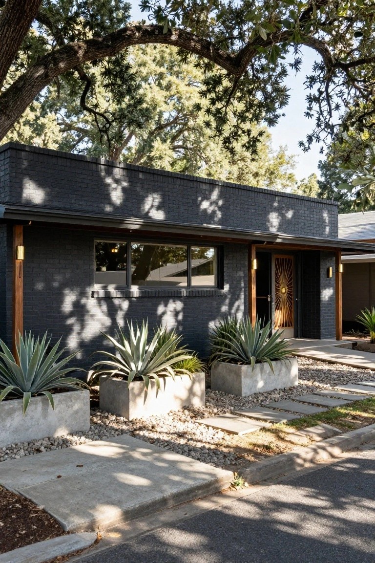 Front exterior of a single-story black brick house with a gold sunburst door, wooden support posts, large windows, agave plants in white concrete planters, gravel ground cover, and concrete pavers under overhanging oak trees.