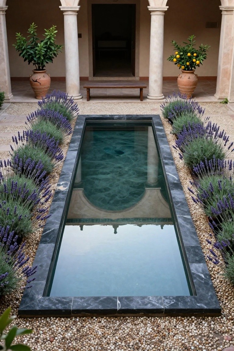 Long narrow black marble reflecting pool in a hacienda courtyard, lined on both sides with purple lavender plants and gravel paths, with stone columns, arched doorway, wooden bench, and terracotta pots of citrus trees.