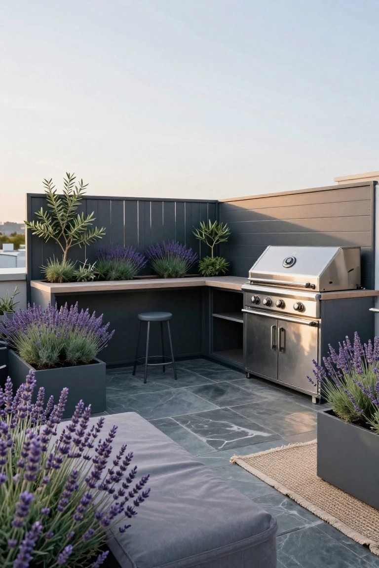 Rooftop terrace with built-in stainless steel gas grill in a gray cabinet base topped by wooden counter and black stool, surrounded by potted lavender and olive trees against dark slatted fencing, on gray tiled floor with cushioned bench and rug.