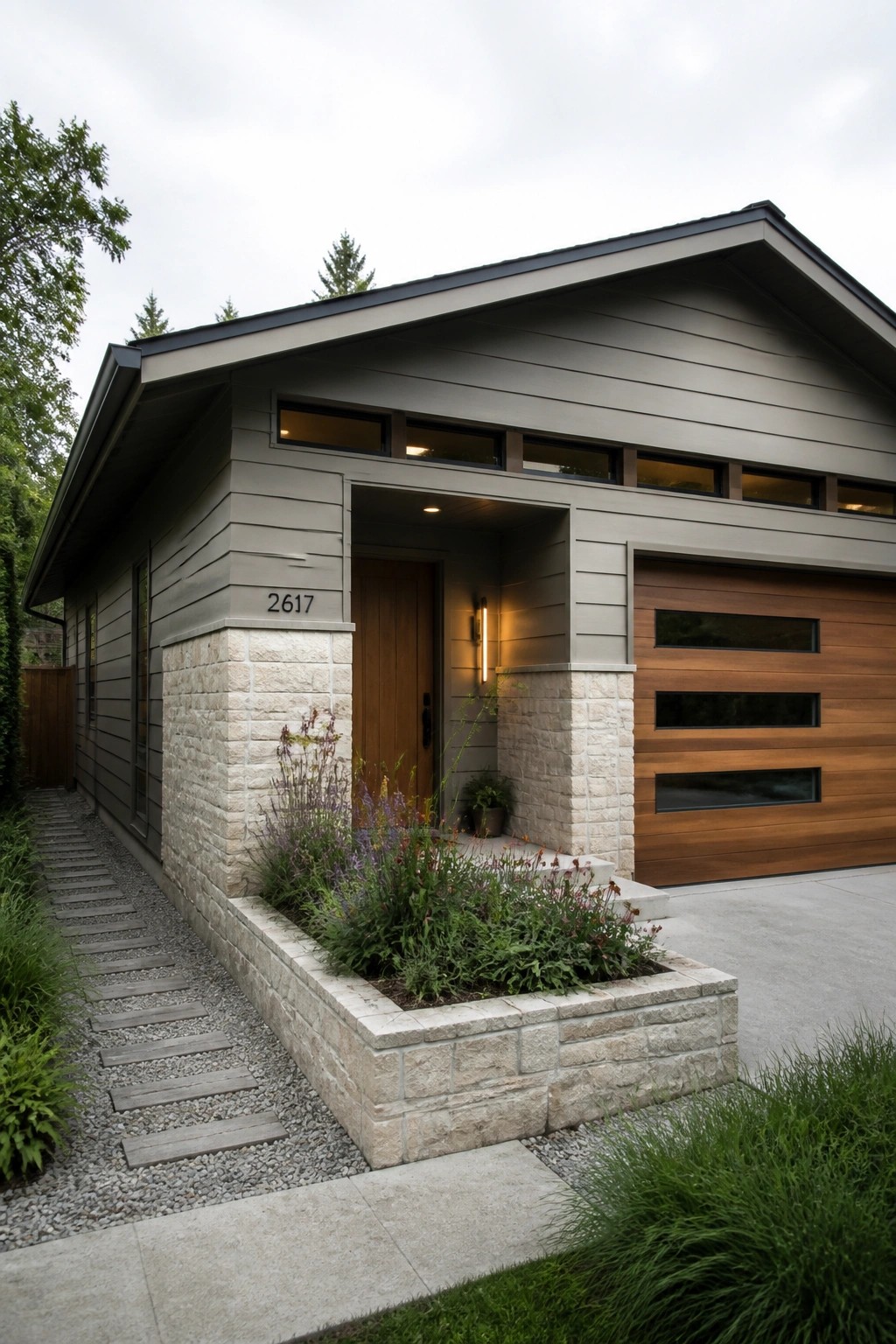A modern single-story house with a low horizontal roof, gray siding, stone base, wooden entry door, and wood garage door.
