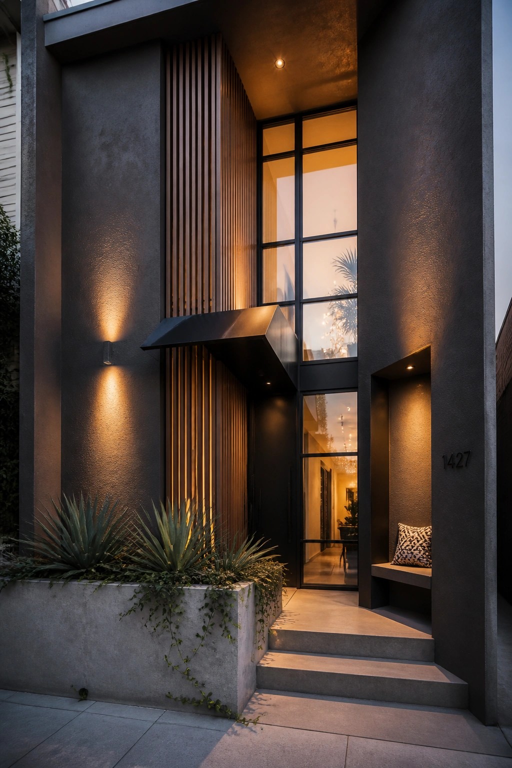 Modern house entrance featuring dark concrete walls, vertical wood slats beside a tall black-framed window, concrete steps, and a recessed bench with a pillow.