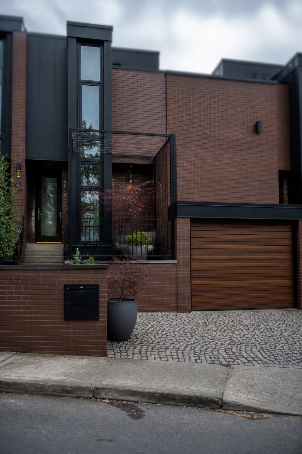 A modern two-story house with red brick walls, black metal window frames and railings, and a horizontal wood garage door.