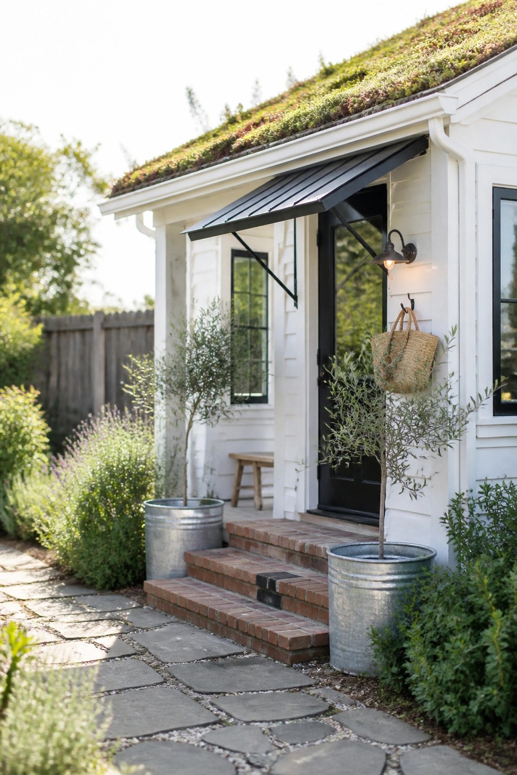 White cottage with black door, green roof, brick steps, metal planters, and stone path.
