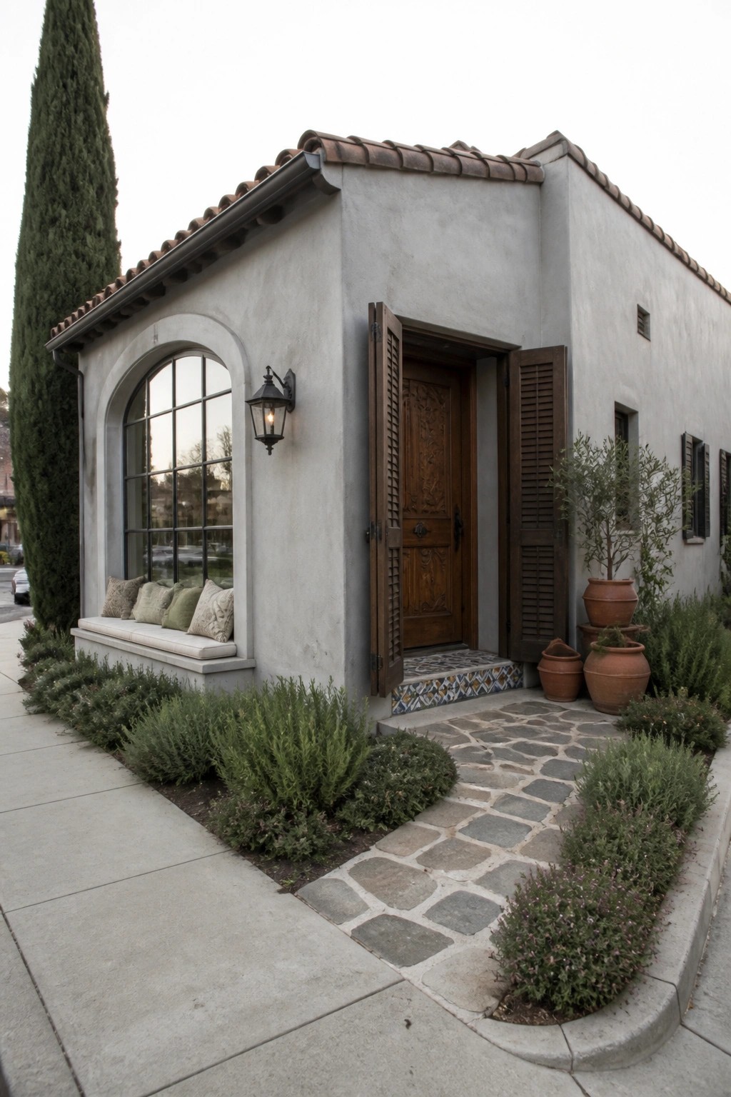 Mediterranean stucco house with arched window seat, carved door, stone path, and potted plants.