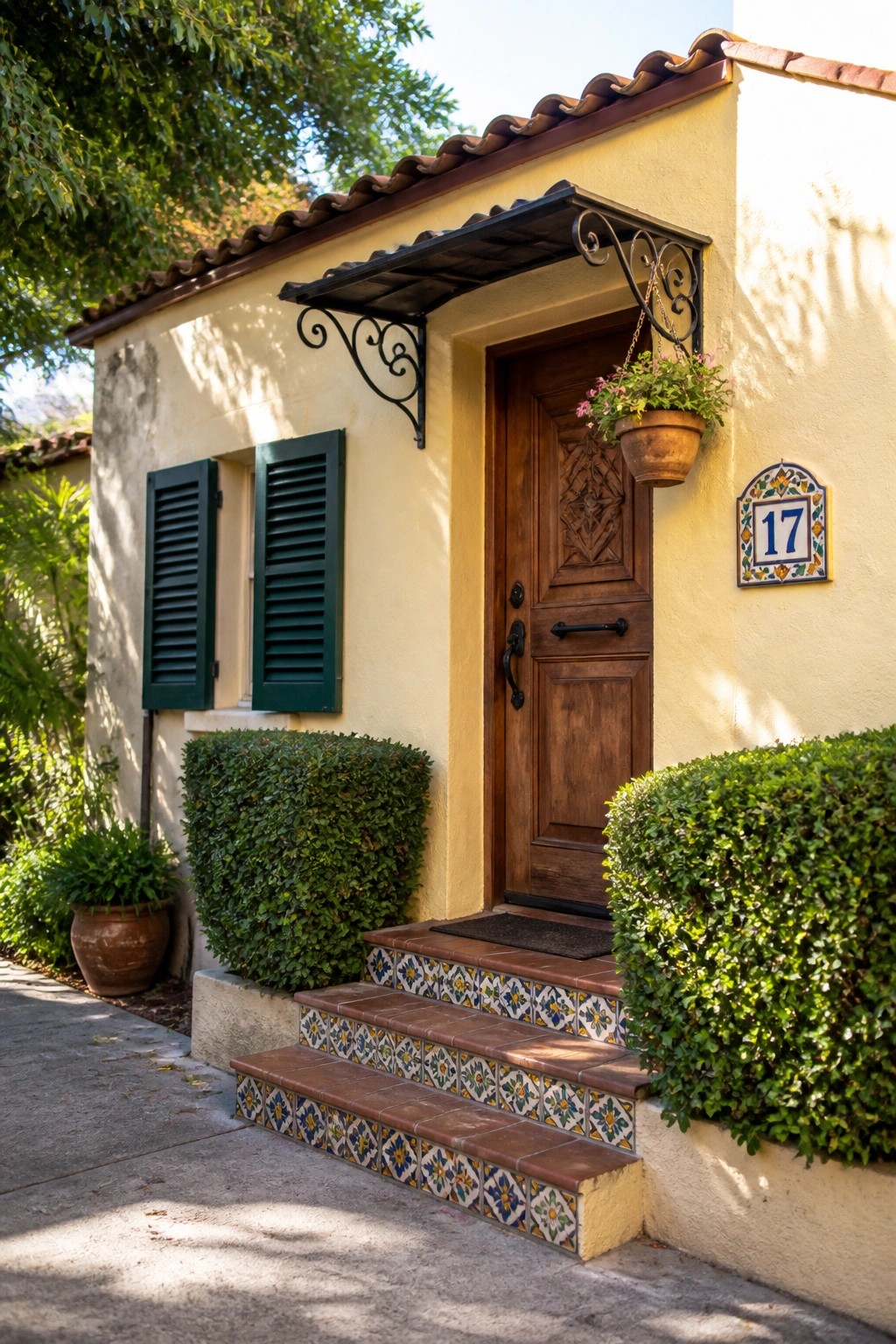 A small stucco house with a wooden front door, colorful patterned tile on the steps, green shutters, and a hanging plant beside the entrance.