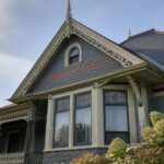 A gray Victorian house exterior with a prominent rounded turret, conical slate roof, and curved bank of windows.