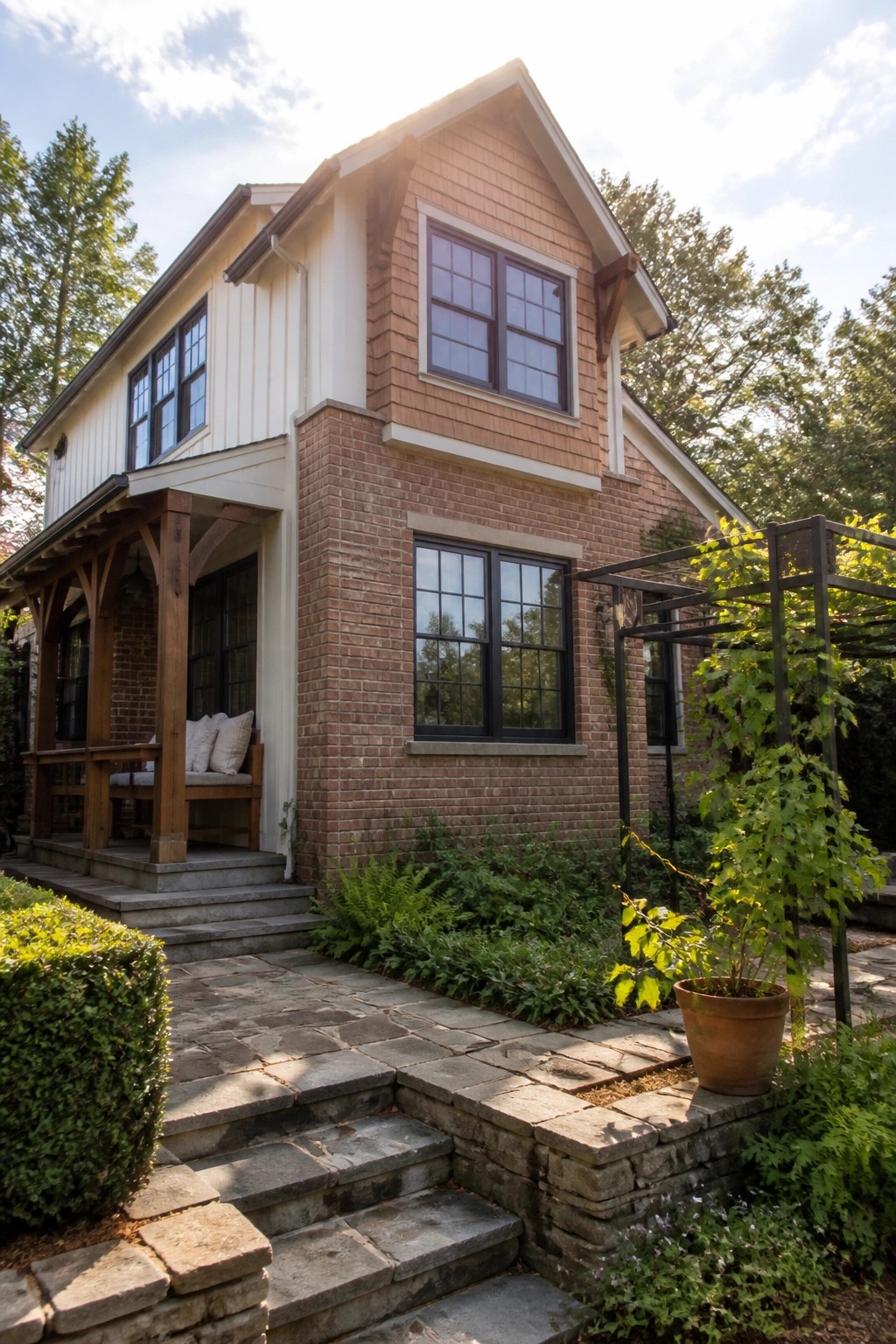 A two-story Craftsman-style house with a brick lower facade, wood shingle siding on the upper level, white trim accents, a wooden front porch, and stone steps leading to a paved walkway with surrounding greenery.