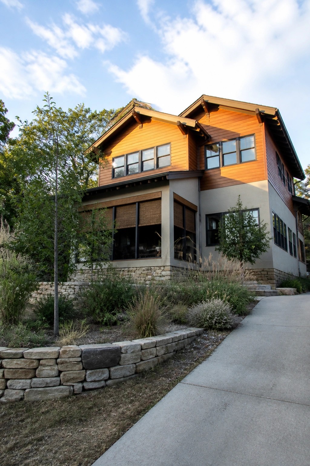 A two-story modern Craftsman house with a stone foundation, warm orange wood siding on the upper levels, and multiple windows.
