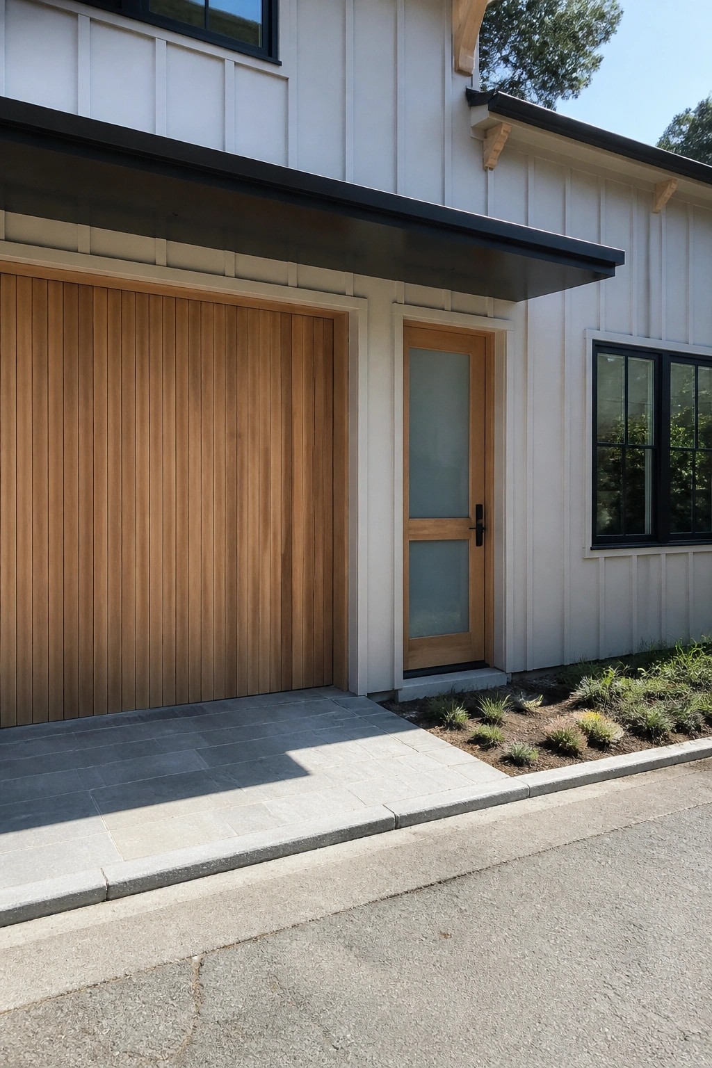 A house exterior featuring a vertical wood garage door beside a wooden entry door with frosted glass panels, set against white siding with a black roof overhang.