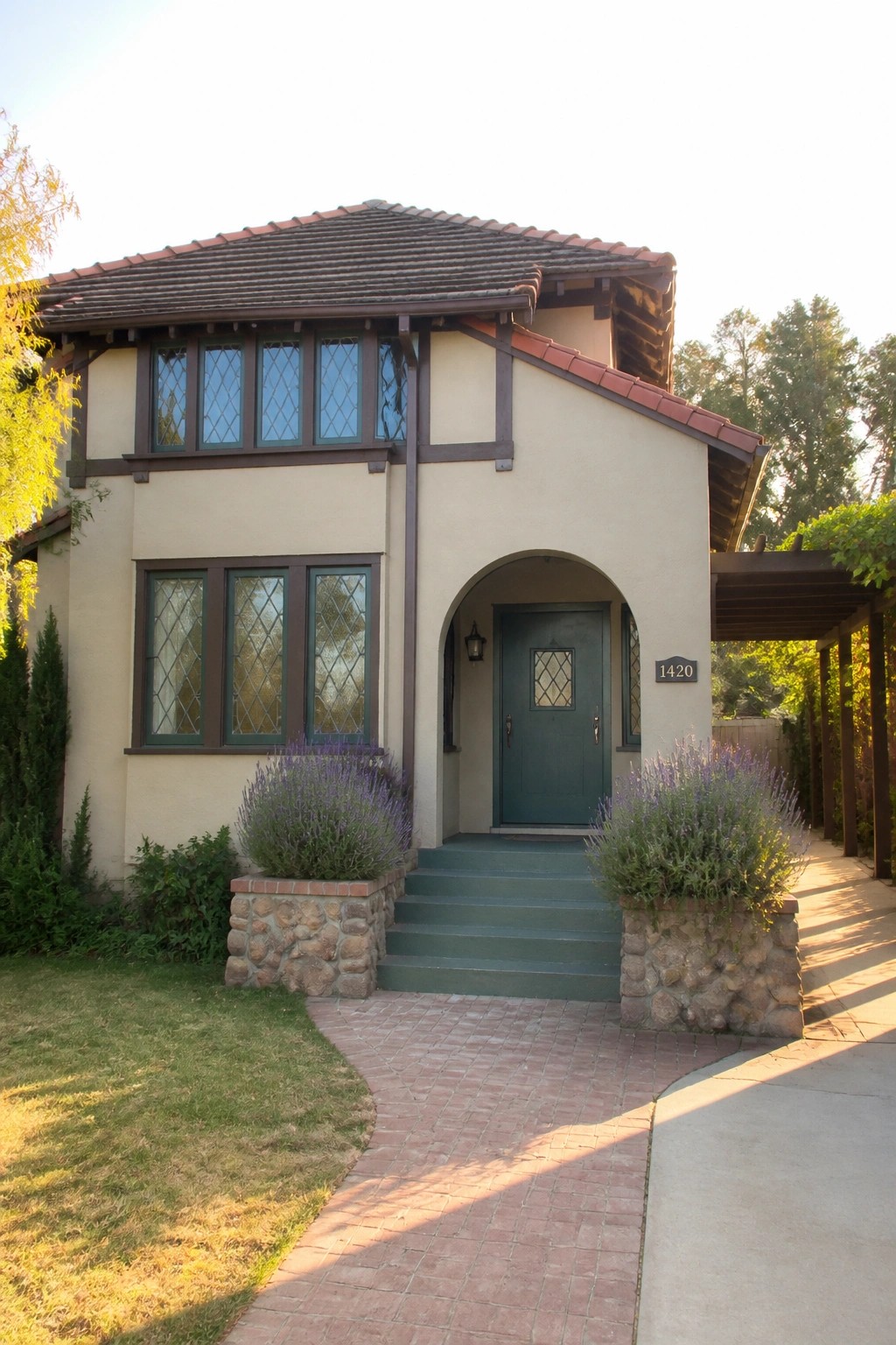 Two-story beige house with red tile roof, green door, and lavender in stone planters.