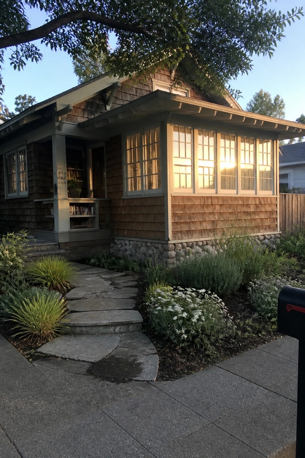 A Craftsman bungalow with wood shingles and a flagstone path curving through garden beds toward the front porch.