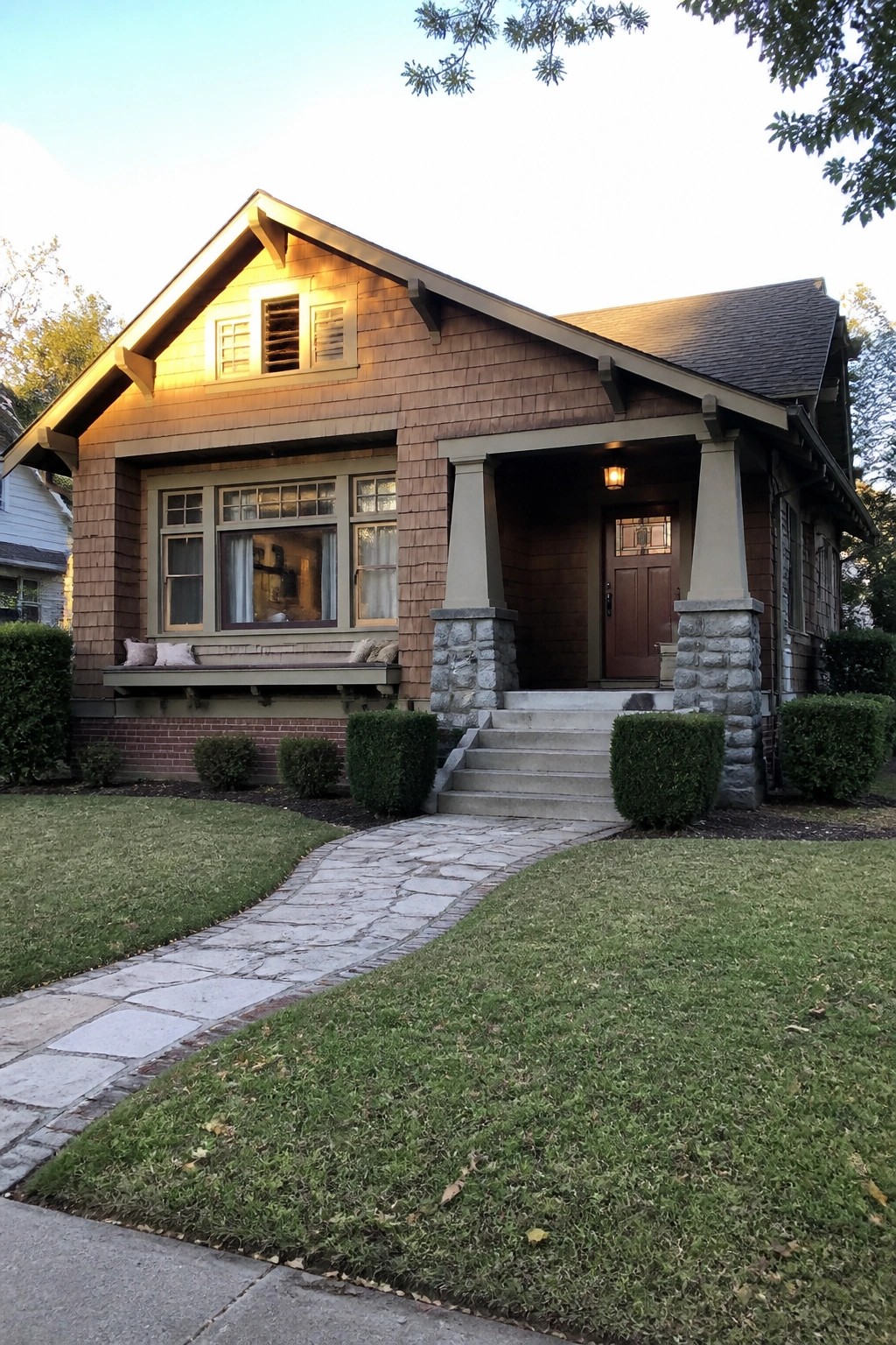 Craftsman bungalow with shingled walls, stone porch pillars, and curved stone path on lawn.