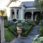 Victorian house with gray siding, flower garden, path, and black iron gate