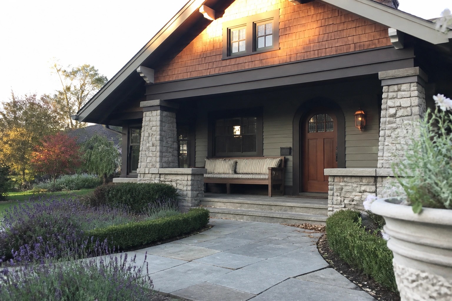 Front view of a Craftsman house with wood shingle siding, stone porch pillars, a covered entry, and a wooden arched door.