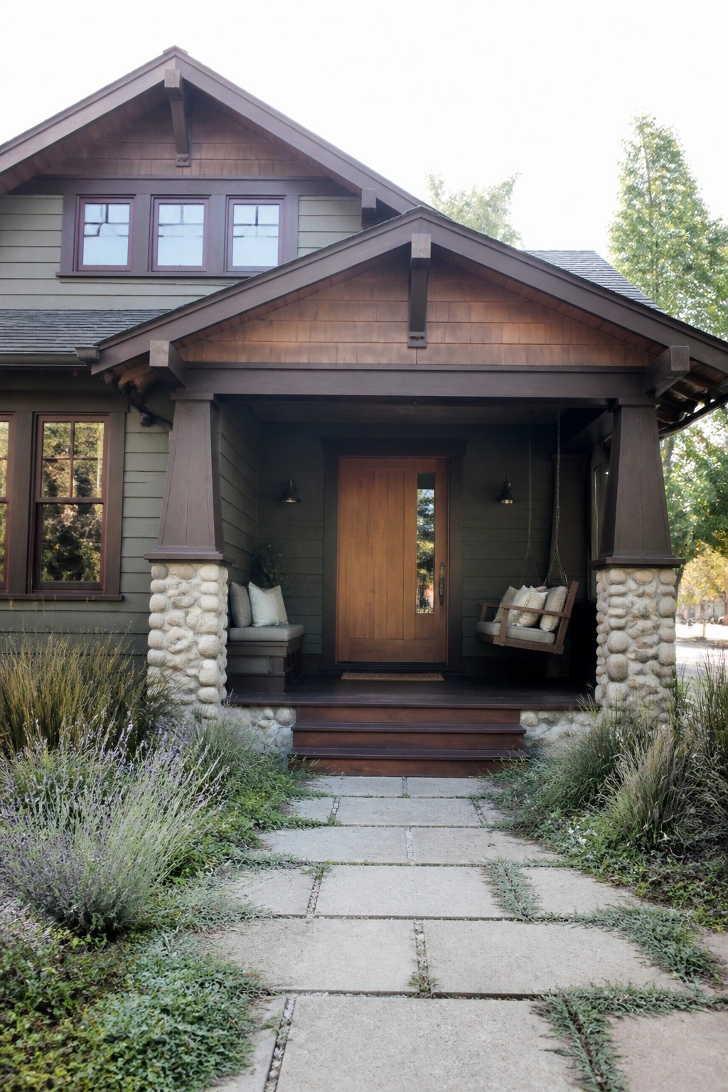 Front view of a Craftsman house with a covered porch supported by dark wood posts on light stone bases, a central wooden door, and a stone path leading to the steps.
