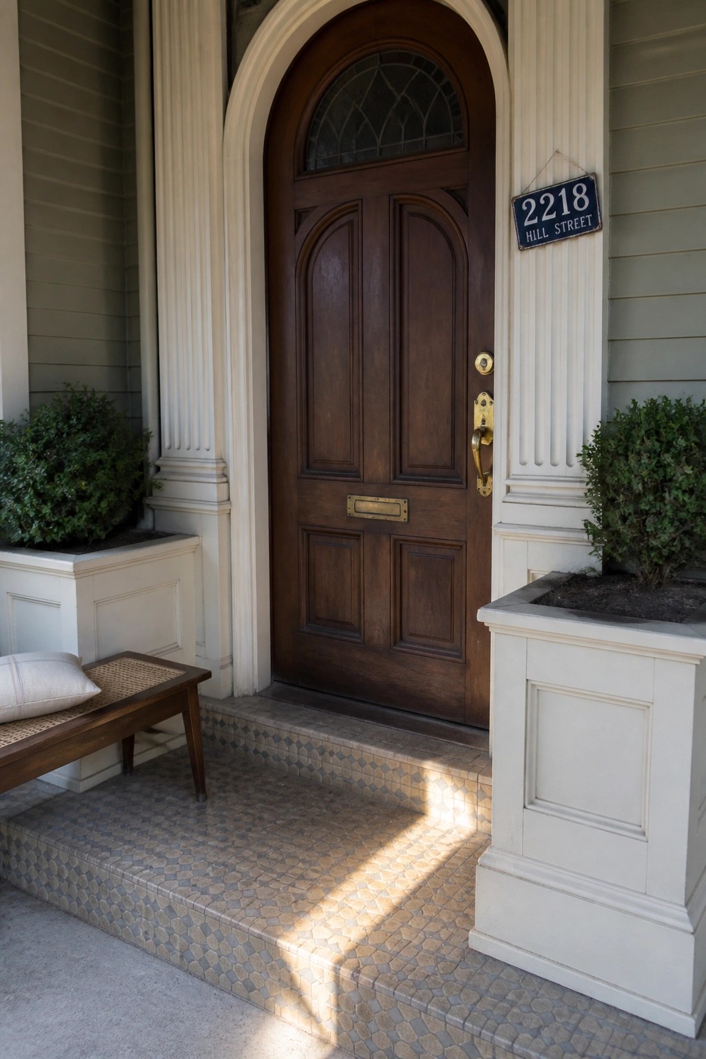 Arched brown wooden door with address sign on columned porch with tiled steps