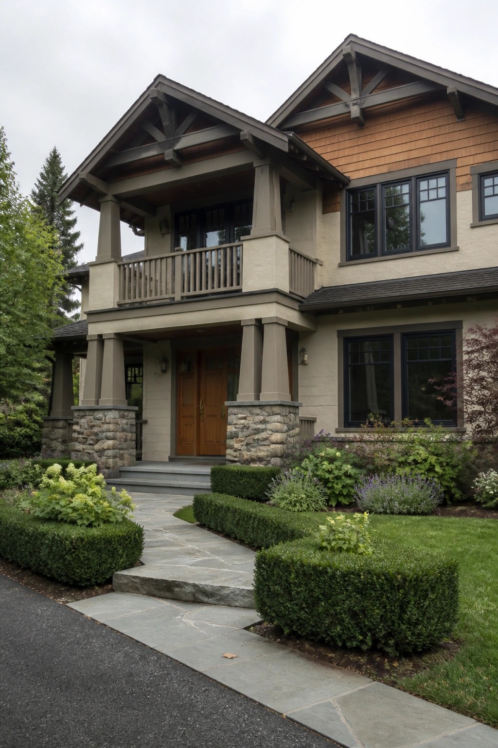 A two-story Craftsman house with a covered front porch supported by large columns on stone piers, a wooden double door, and an upper balcony with railings.