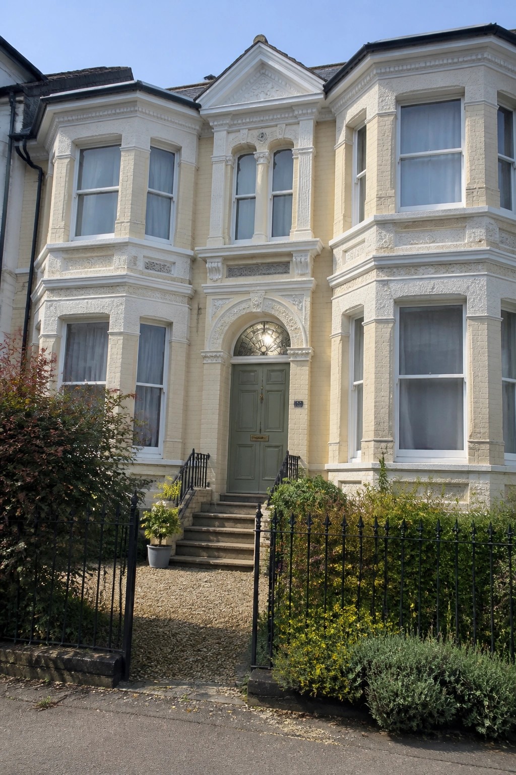 Brick Victorian townhouses with white bay windows and front gardens on sunny street
