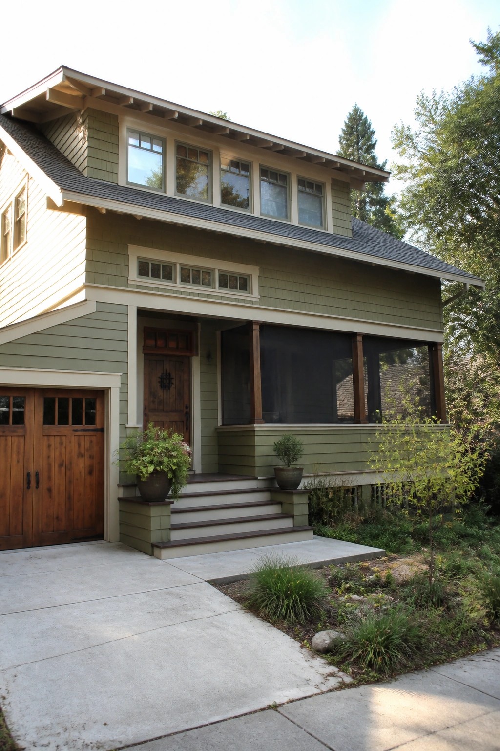 Front view of a green Craftsman house with a wide covered porch supported by tapered columns, wooden front door, and concrete steps leading to the entry.