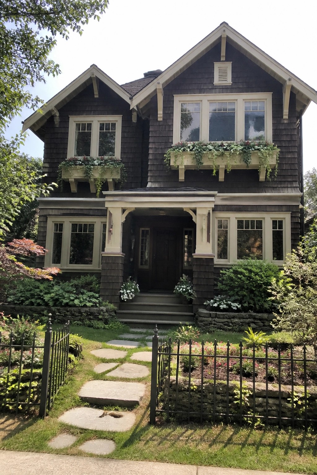 A two-story dark gray Craftsman house with a central covered porch, white window trim, flower boxes, and a stone base.
