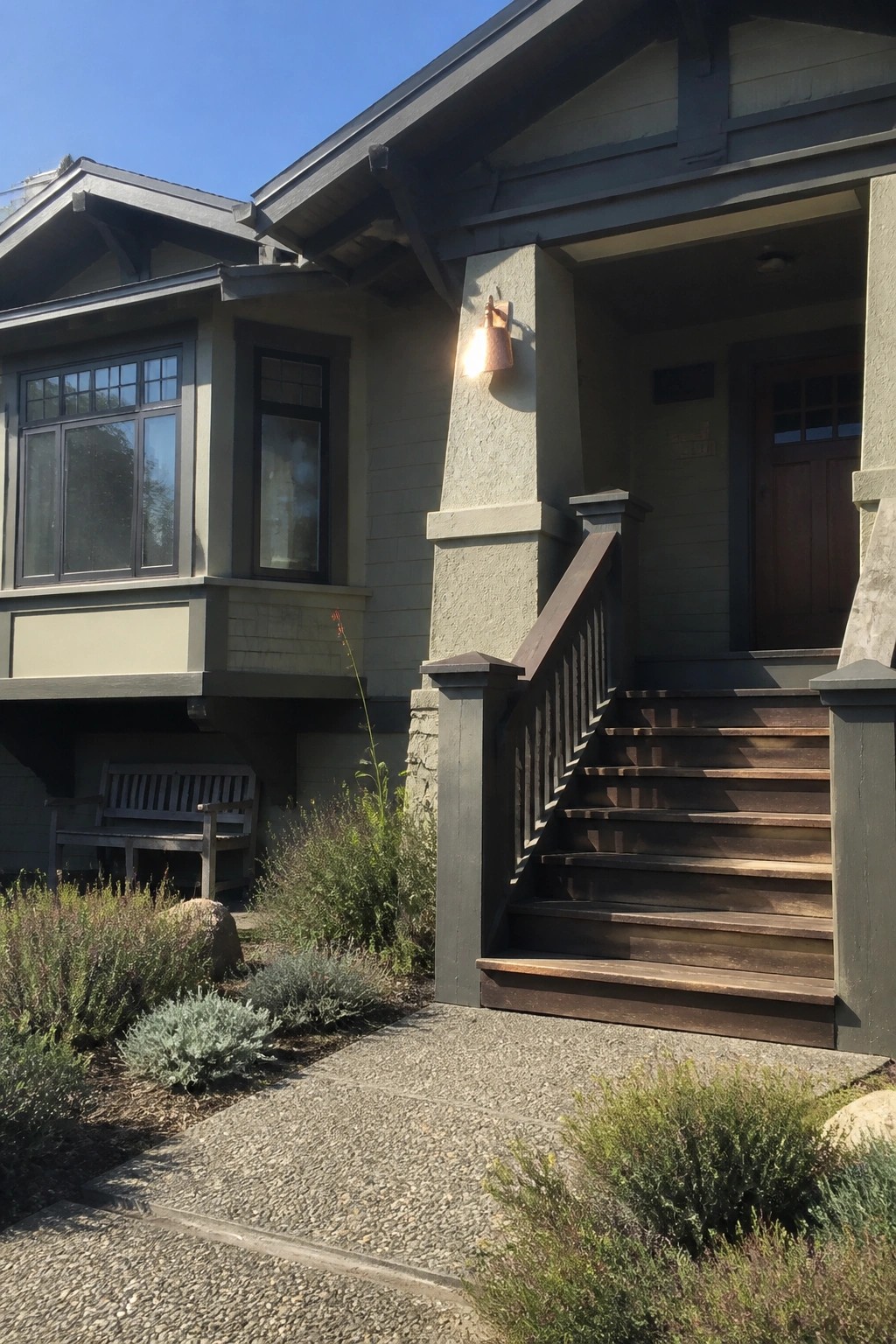Craftsman house entrance with wooden stairs, porch light, windows, and garden bench