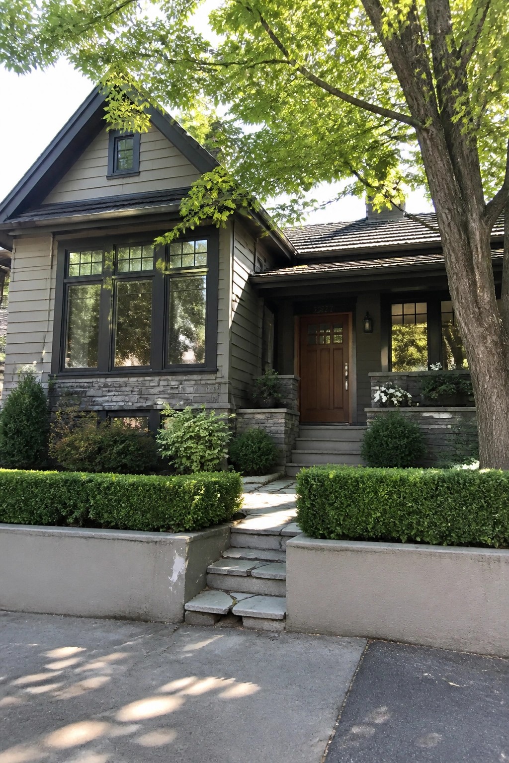 Gray house with stone steps, wooden door, large windows, and green hedges.