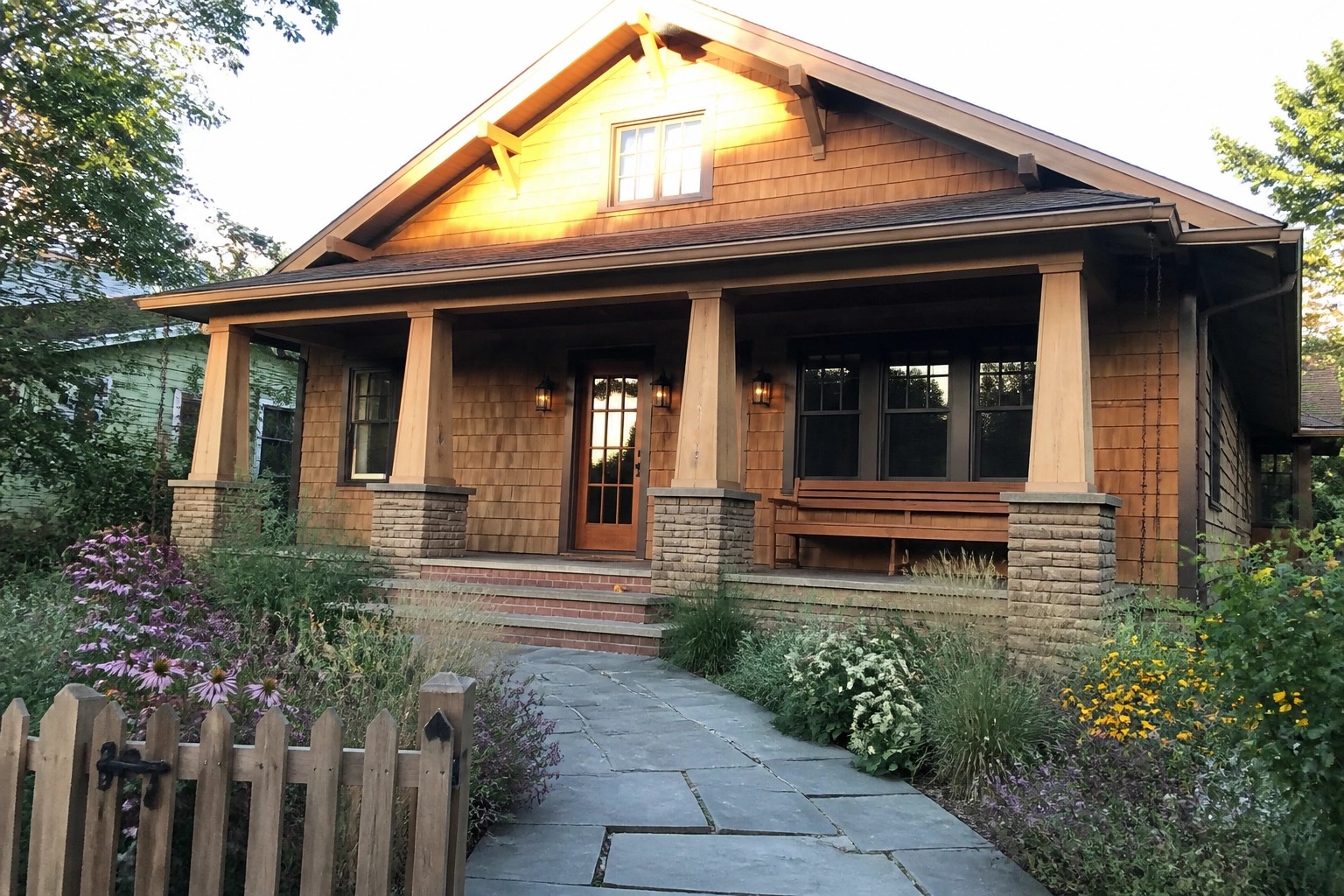 Wooden craftsman house with stone porch, brick steps, and flower-lined slate path