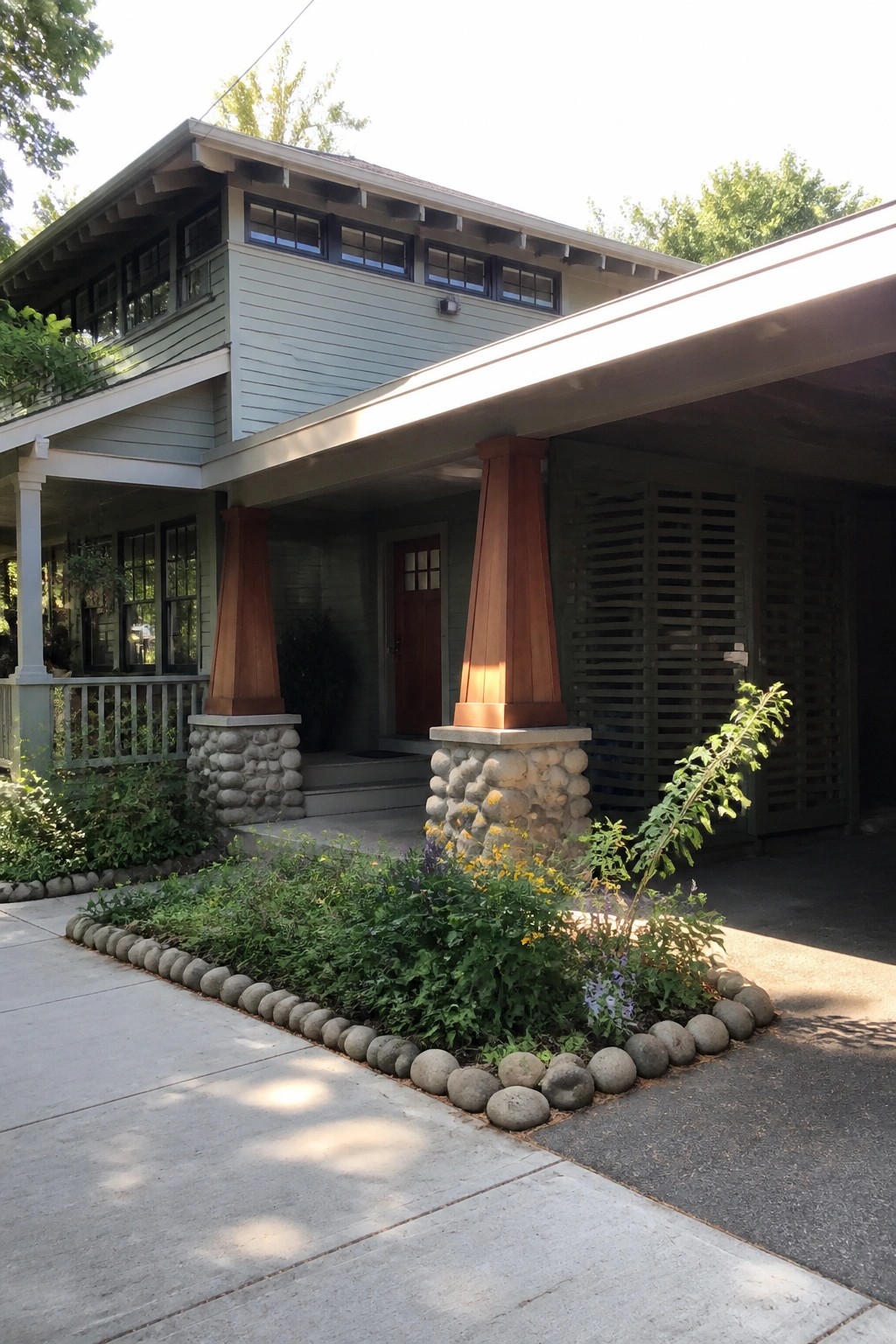 Front view of a Craftsman house porch with two tapered wood columns resting on rough stone bases and a curved garden bed edged in matching stones.