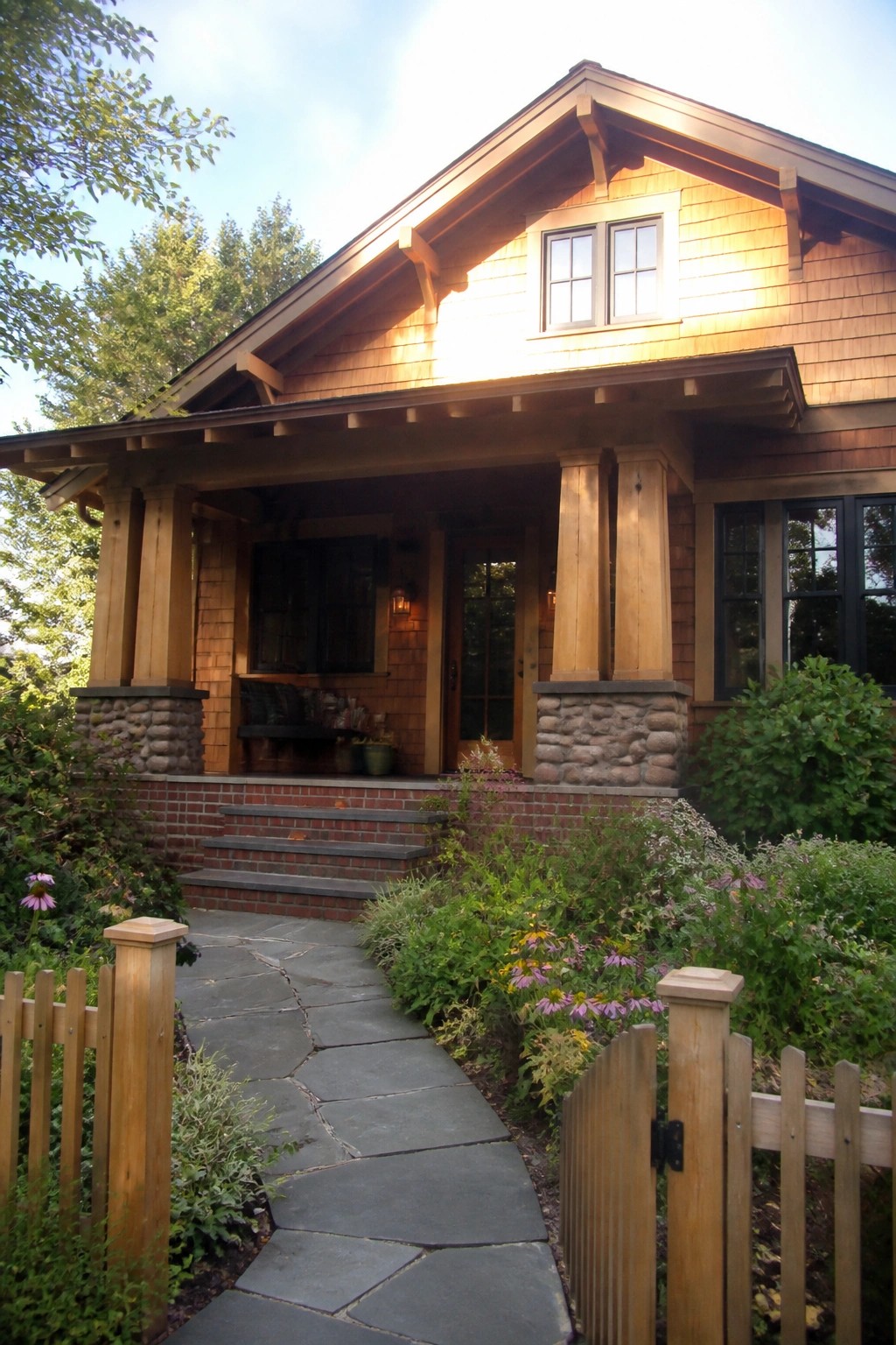 Wooden craftsman house with stone porch, brick steps, and flower-lined slate path