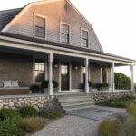 Large shingled house with white porch columns, black door, and stone steps.