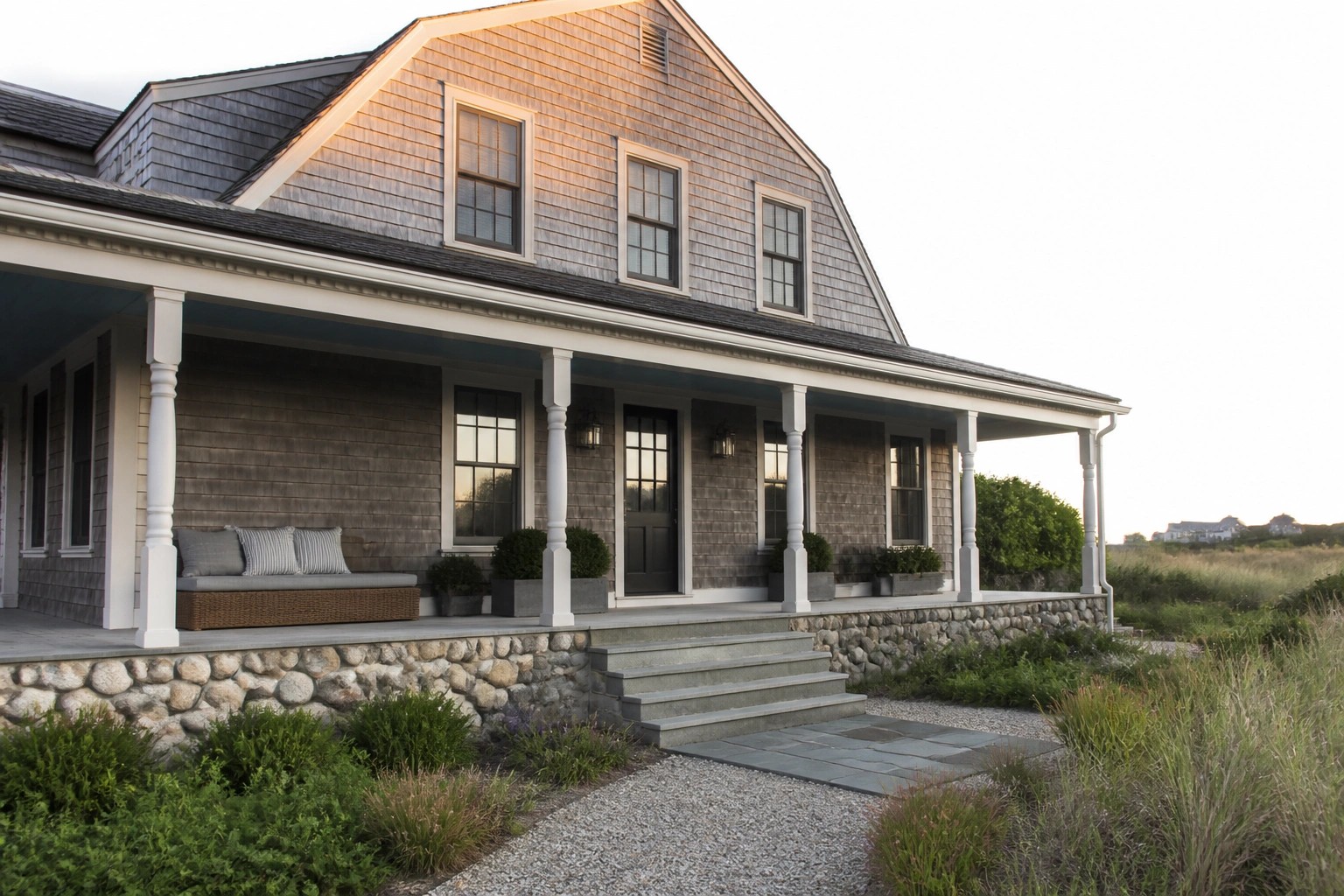 Large shingled house with white porch columns, black door, and stone steps.